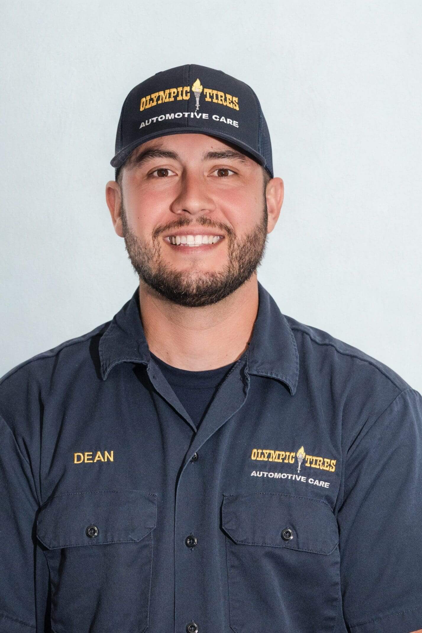Smiling man in a navy blue uniform and cap, embroidered with 'DEAN' and a company logo.
