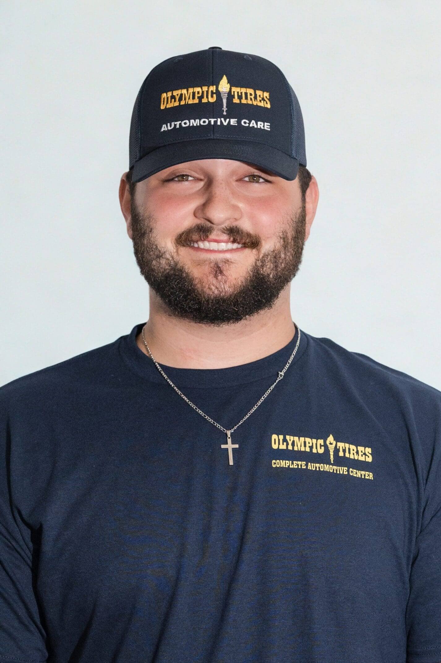 Smiling man wearing a navy blue shirt and black cap with a cross necklace.