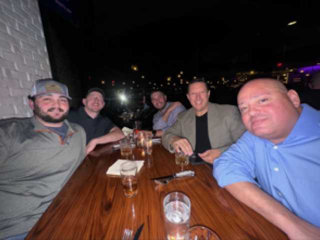 A group of five men sitting around a wooden table at night.