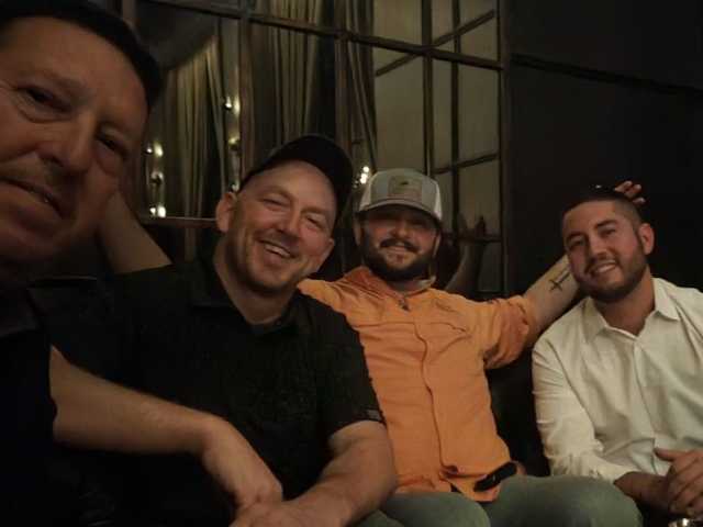 Four men sitting together, smiling in a dimly lit room.
