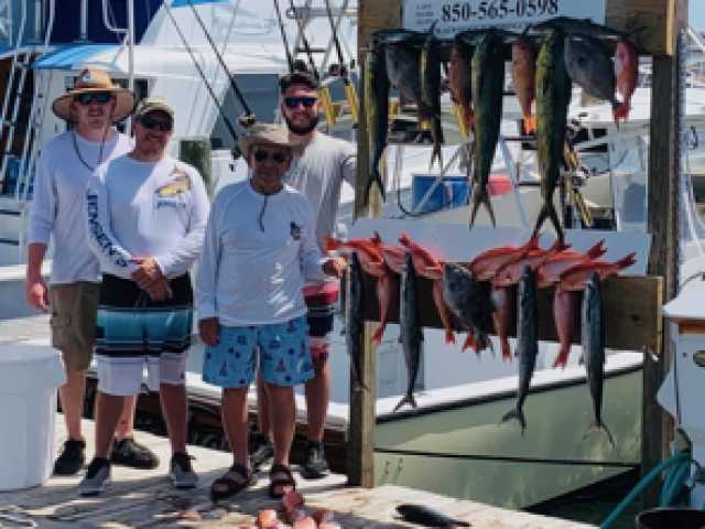 Group of men posing with their freshly caught fish on a dock beside a boat.