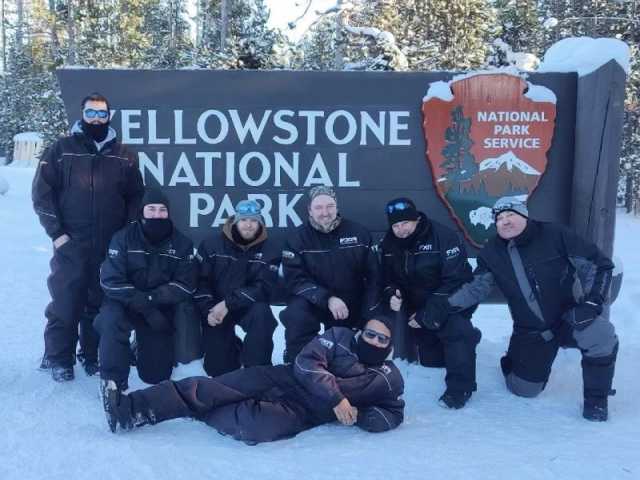 Group posing in front of Yellowstone National Park sign during winter.