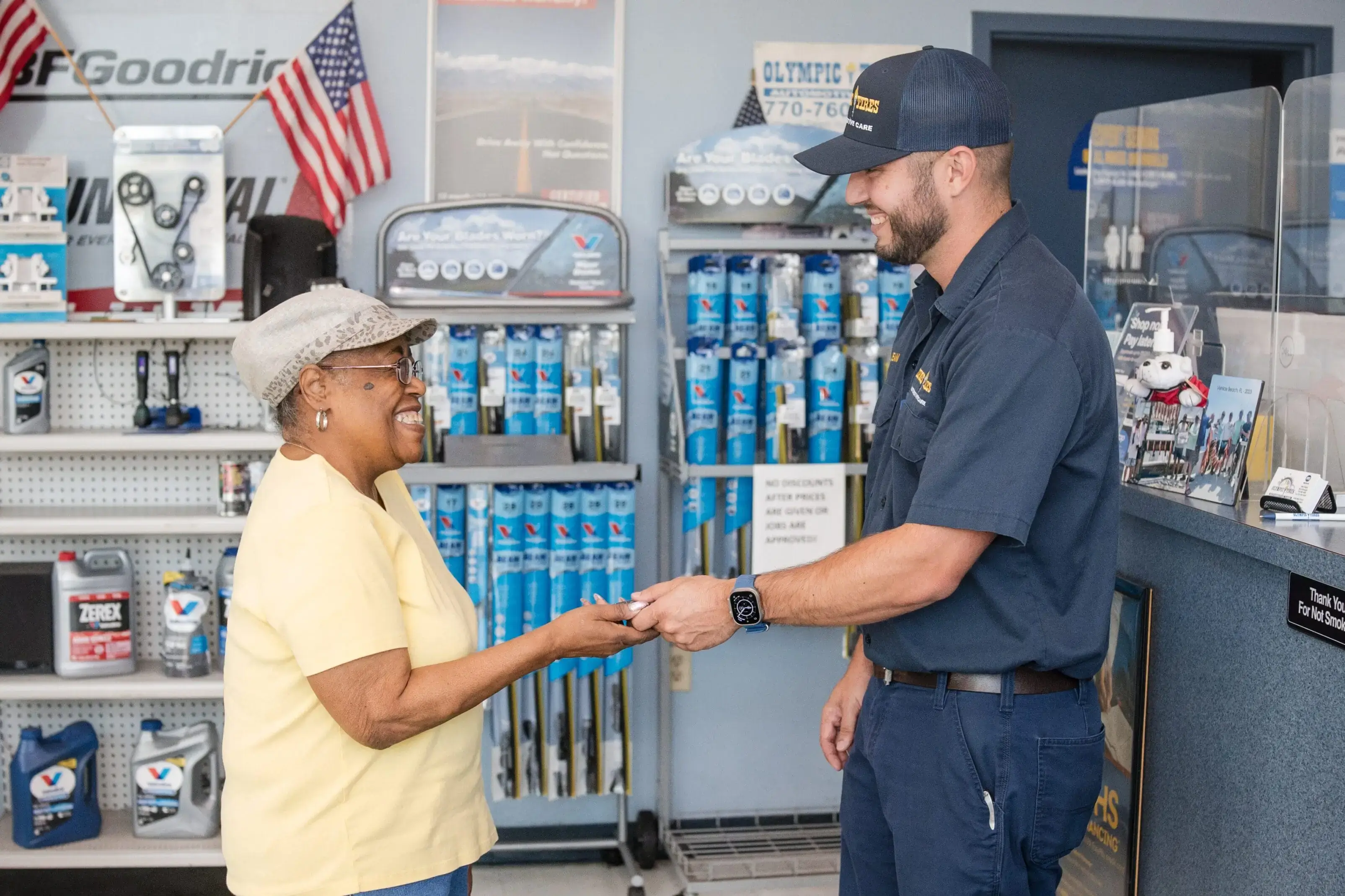 A delivery man hands a package to a smiling elderly woman in a store.