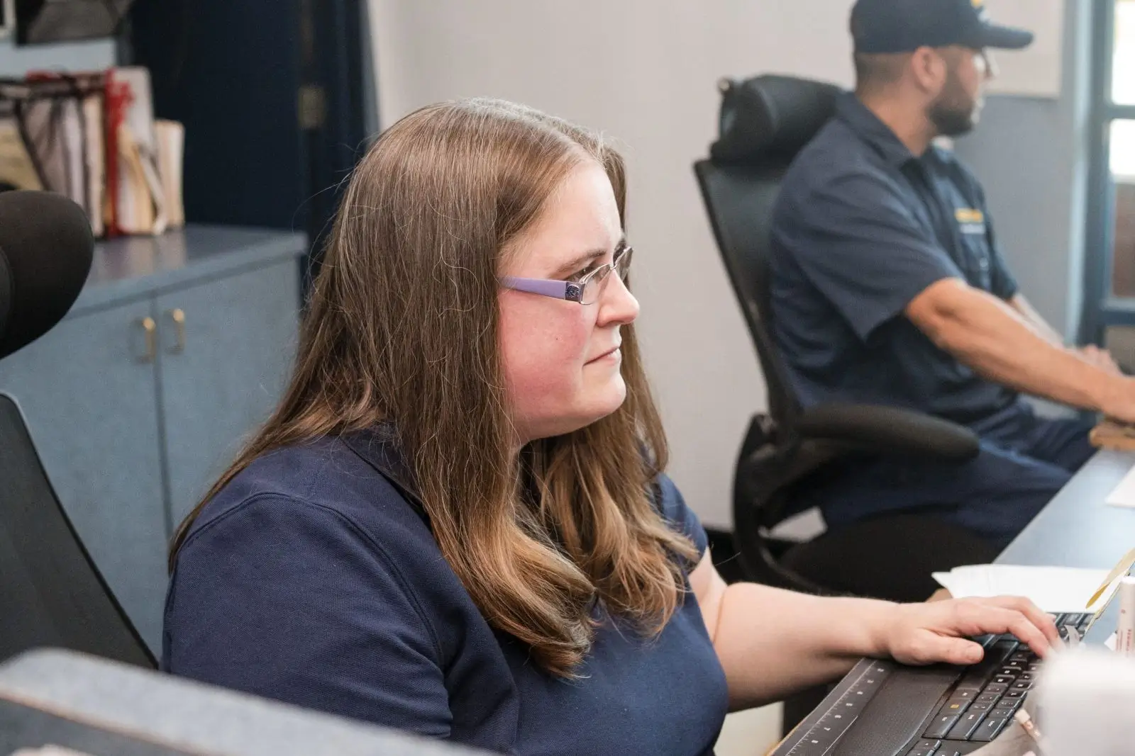 A woman with glasses focusing on her computer screen in an office.